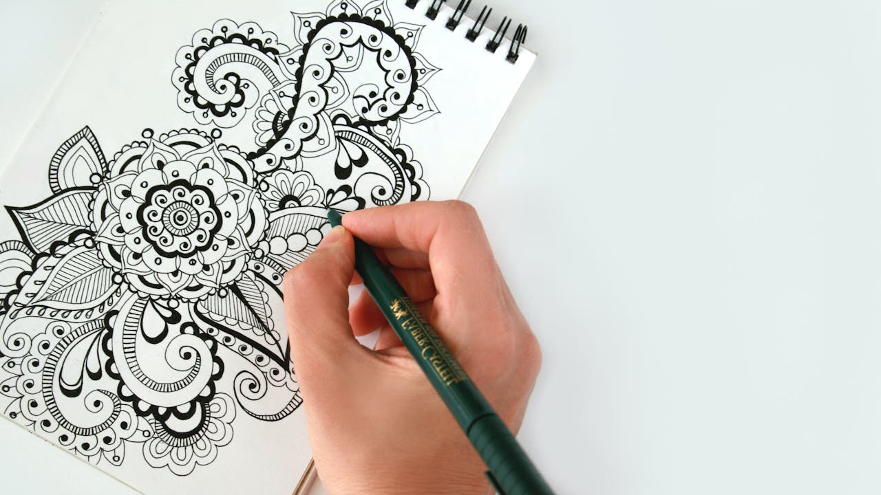 An open sketchbook with drawings beside pencils and art tools