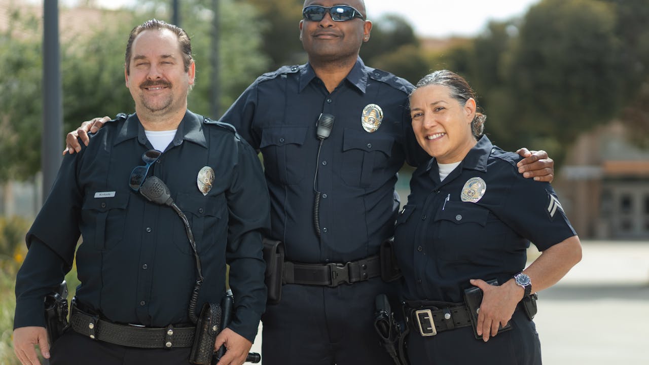 Three smiling police officers in uniform standing together outdoors